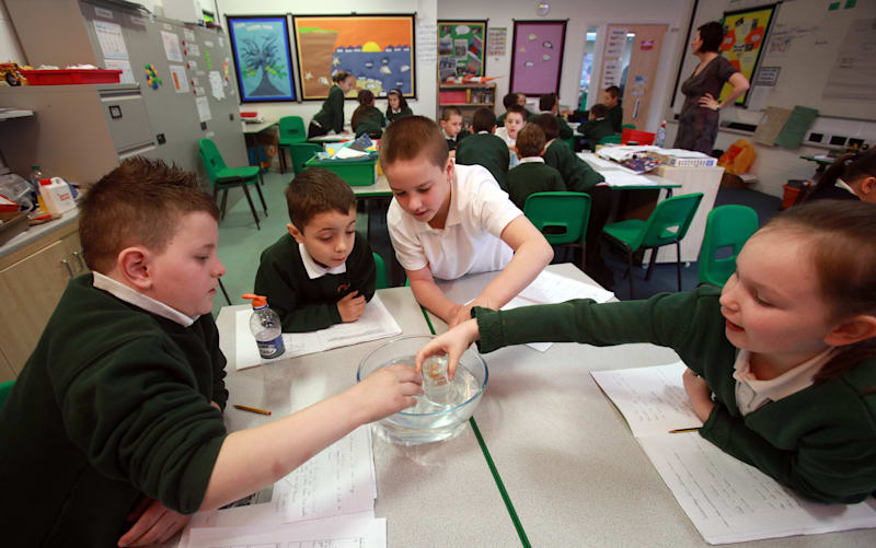 Primary school students in the UK in a classroom sit at a table playing with water