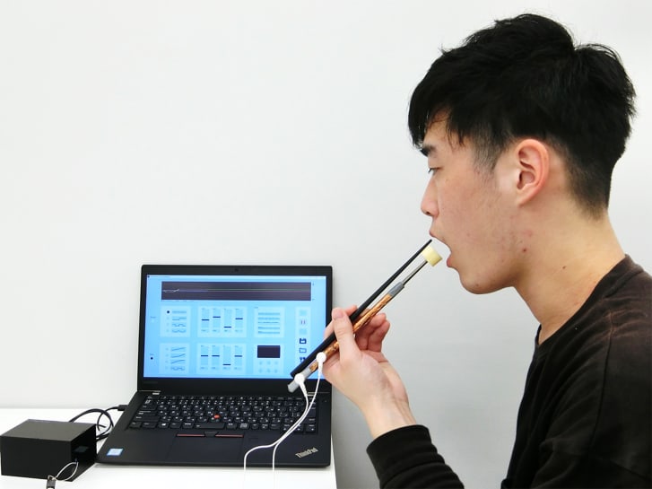 An employee of Kirin Holdings demonstrates chopsticks that can enhance food taste using an electrical stimulation waveform that was jointly developed by the company and Meiji University's School of Science and Technology Professor Homei Miyashita, in Tokyo, Japan.