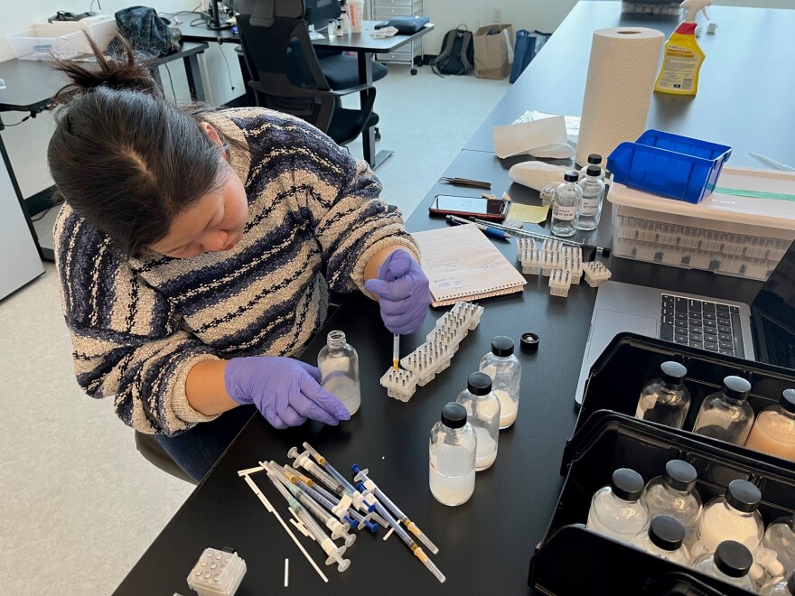 A woman with black hair and a striped sweater fills vials with a pipette