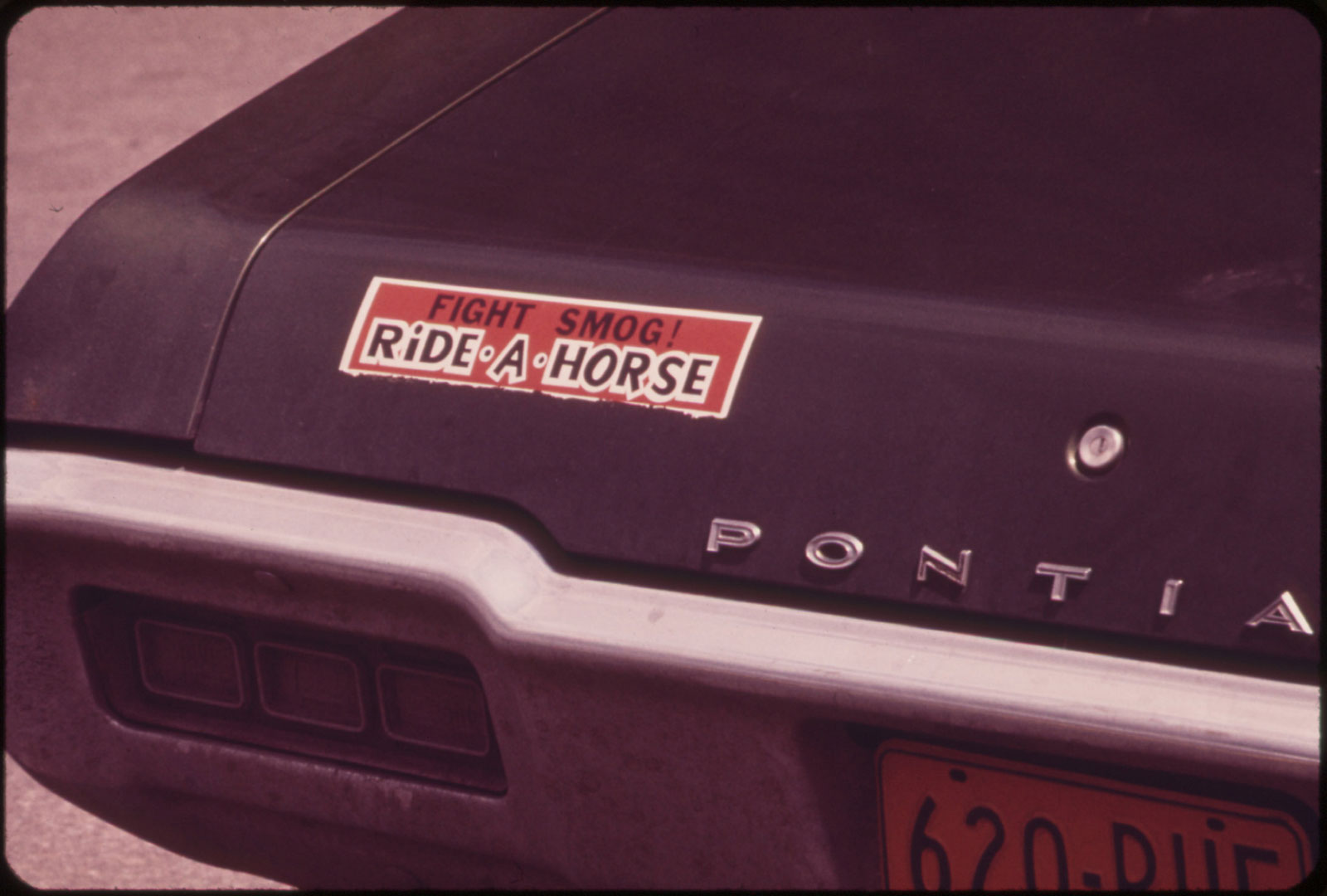 1973 photo of close up of rear end of Pontiac car with bumper sticker reading "Fight smog! Ride a horse"