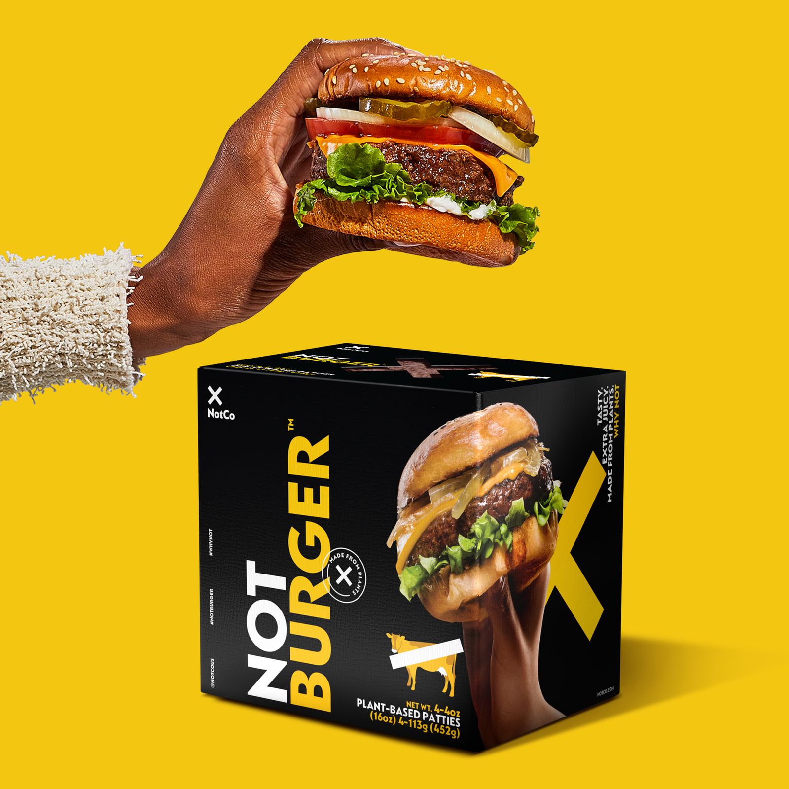 A hand holds a NotBurger above a NotBurger box on a yellow background.