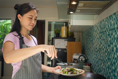 Asian woman holding tasty cook dishes in the kitchen.Smelling delicious seafood noodle with vegetab...