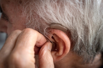 Older adult man inserting a hearing aid into his ear.