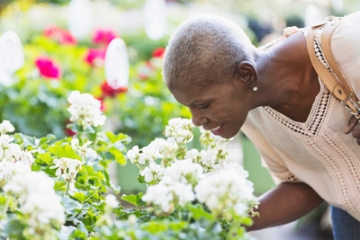 Older adult woman smelling flowers at a garden center.