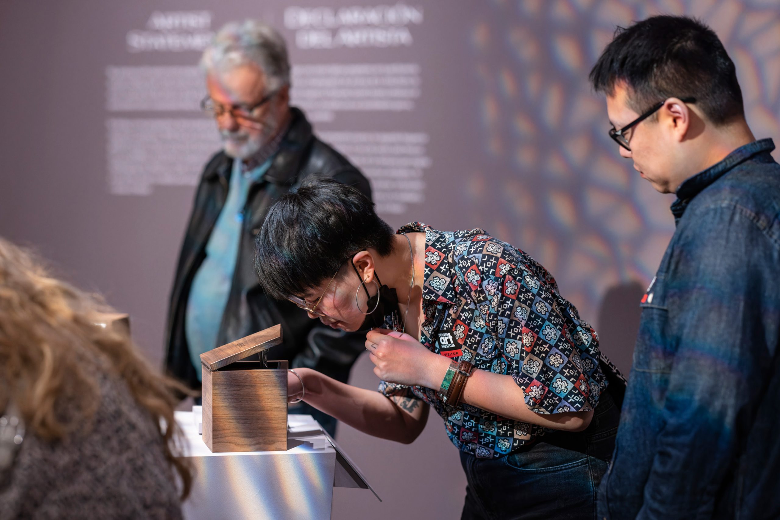 a woman bends over to sniff a scent in a box with other visitors nearby in the Near East to Far West exhibition
